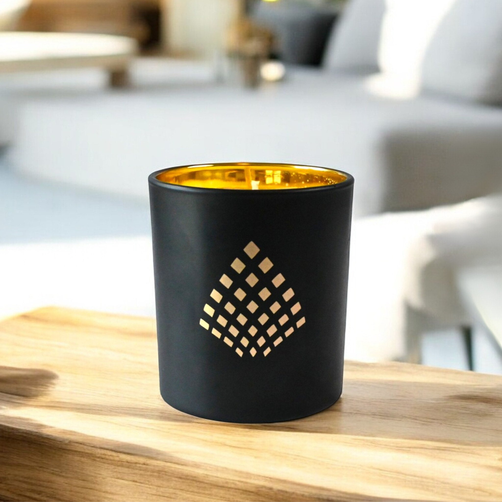 Black and gold luxury candle placed on a wooden surface in a bright, modern living room setting, illuminated by natural light