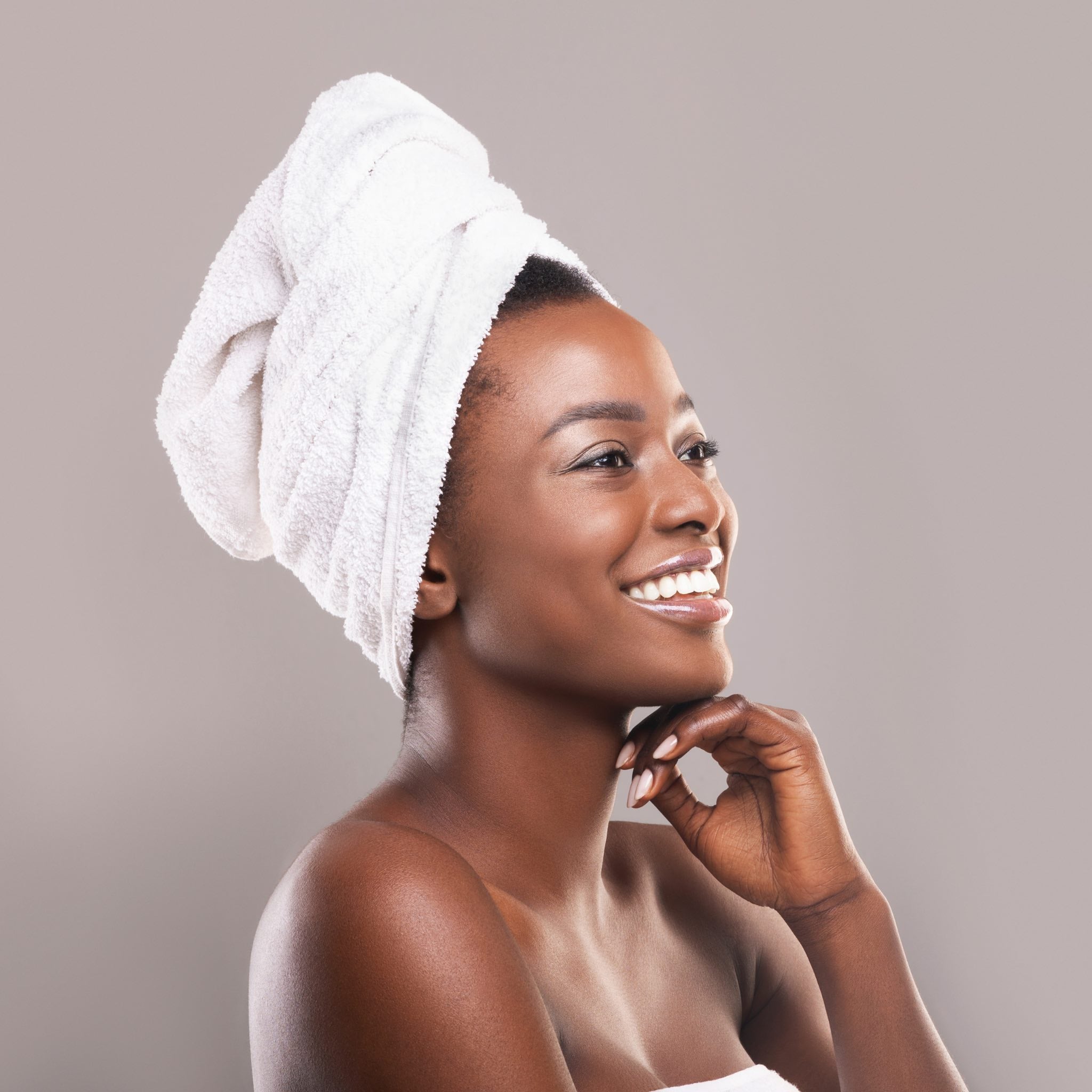 Smiling woman with a towel wrapped around her head, radiating post-bath relaxation and glowing skin, looking content and refreshed.