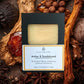 Goat's milk face and body soap bar in a black box with 'Amber & Sandalwood' scent, surrounded by natural elements.