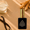 A black perfume bottle with vanilla beans and a glass of milk nearby.