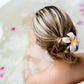 A woman with a flower in her hair relaxing in a bath filled with water and scattered flower petals.