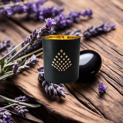 A black and gold Couture Home & Body candle set against surrounded by lavender sprigs on a wooden surface, evoking a calming and natural ambiance.