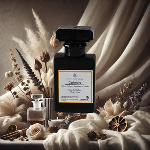 A perfume bottle labeled "Cashmere" by Couture Home & Body is displayed against a soft, neutral-toned background with draped fabric and dried botanicals, evoking warmth, elegance, and comfort.