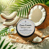 The image features a tin of Coco Cream 100% Organic Lip Balm from Couture Home & Body, set against a tropical backdrop with a cracked coconut, coconut cream, and palm leaves. The scene emphasizes the natural ingredients and soothing qualities of the product, evoking a fresh and tropical feel.