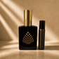Black perfume bottle and rollerball with gold accents in warm sunlit setting.