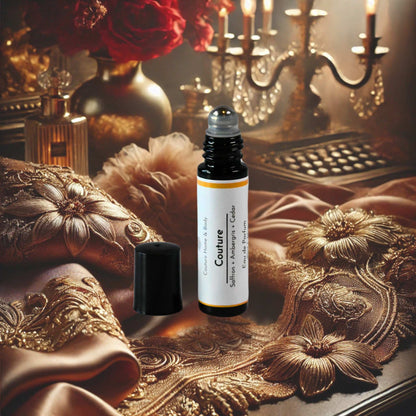 A rollerball perfume labeled "Couture" by Couture Home & Body is displayed on an elegant surface with intricate fabric details, soft lighting, and a luxurious backdrop of candles and red roses, evoking sophistication and luxury.