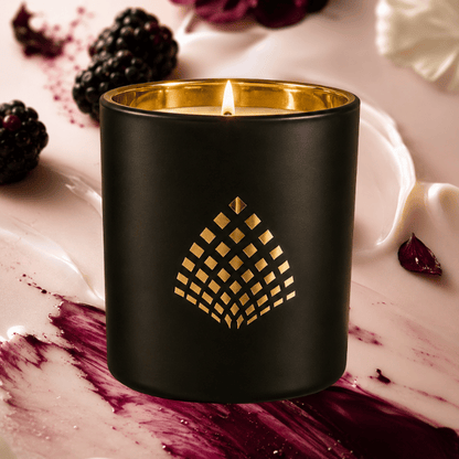 Black candle with gold lid and decorative pattern on a marble surface with berries and buttercream.