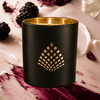 Black candle with gold lid and decorative pattern on a marble surface with berries and buttercream.