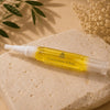 Cuticle oil pen on a textured beige stone with dried flowers and green leaves in the background.