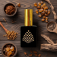 Perfume bottle with gold cap on a wooden surface with amber-colored ingredients.