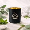 Black candle with gold interior on a white surface with spa elements.
