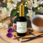 Bottle of 'Golden Hour' room and linen mist with flowers, figs, and a cup of tea on a wooden surface.