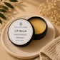 An open jar of lip balm with pale yellow balm visible inside, placed on a round beige stone dish.