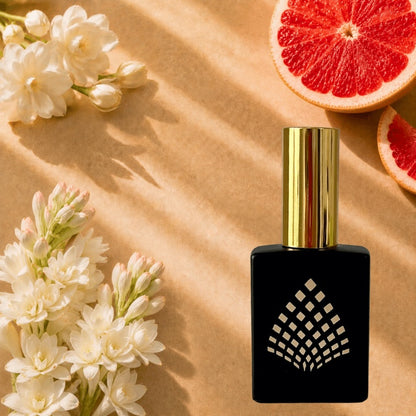 A black perfume bottle on a tan paper background, styled with white flowers and sliced grapefruit.