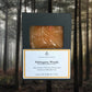 Bar of soap in packaging with 'Mahogany Woods' label against a forest background.
