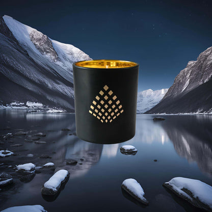 A black and gold Couture Home & Body candle set against a backdrop of snowy mountains and a calm, reflective lake at night capturing the essence of the Nordic Night candle.