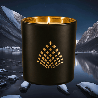 Black luxury candle with gold interior set against a snowy mountain lake at night.