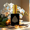 Perfume bottle with gold cap and black body featuring a geometric design, surrounded by white orchids and vanilla beans.