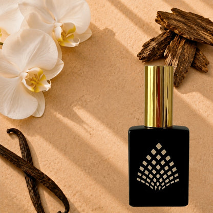 A black perfume bottle on a textured beige surface with white orchids, vanilla beans, and oud pieces.