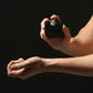 Close-up of a person spraying perfume on their wrist from a sleek black bottle, set against a dark background for a minimalist and elegant look.