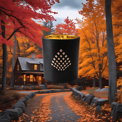 Black candle with gold interior in front of a cozy cabin in the woods during autumn.
