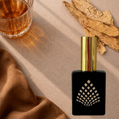A black perfume bottle on a beige surface with a glass whiskey, suede, and tobacco leaves.