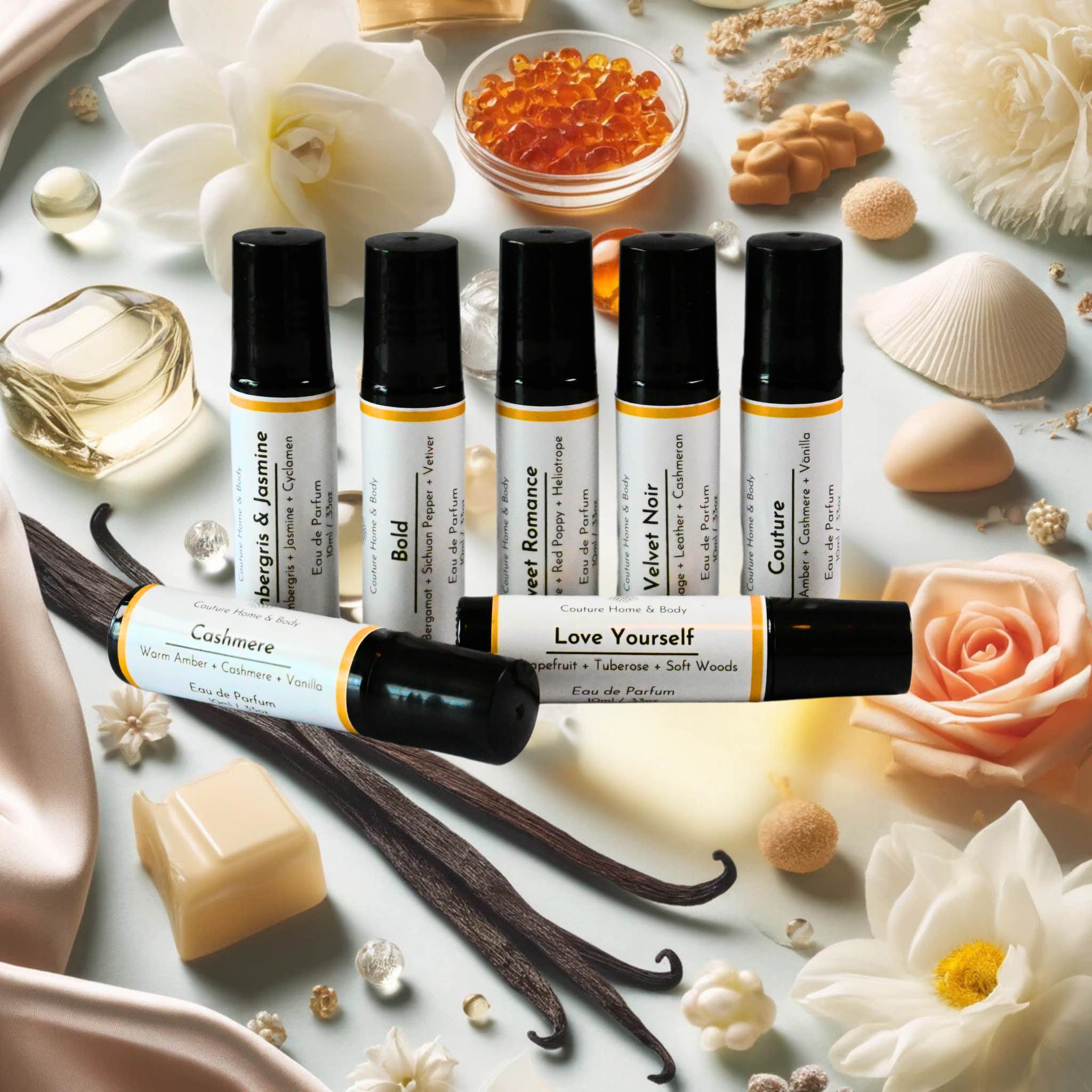 A collection of rollerball perfumes by Couture Home & Body displayed on a bright, elegant background with vanilla pods, amber stones, flowers, and pearls, highlighting the luxurious and diverse ingredients of the fragrances.