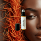 Bottle of Saffron Skin perfume with a close-up of a woman's face and orange threads.