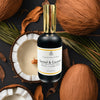 Bottle of Santal & Coconut room and linen mist surrounded by coconuts and leaves on a dark background.