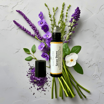 Rollerball perfume labeled 'Seven Stems' surrounded by lavender flowers and green leaves on a textured white background.