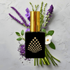 Perfume bottle with gold cap and black base against lavender flowers and green leaves.