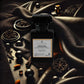 A perfume bottle labeled "Velvet Noir" by Couture Home & Body is displayed against a dark, luxurious background with rich textures of leather and satin, evoking a sense of mystery, elegance, and intrigue.