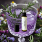 Violet gin bottle with a glass of purple liquid and rosemary garnish, surrounded by flowers.