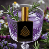 Perfume bottle with gold cap and black square design in a purple glass with rosemary and flowers.