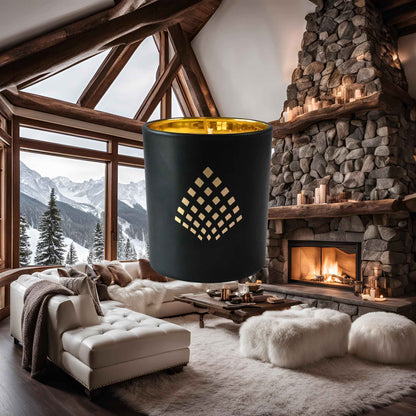 A black and gold Couture Home & Body candle set against a luxurious mountain chalet with a stone fireplace, plush seating, and snowy views, evoking the warm, cozy ambiance of the Winter Chalet candle.