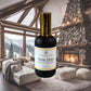 A bottle of "Winter Chalet Room + Linen Mist" by Couture Home & Body, displayed in front of a luxurious winter cabin scene. 